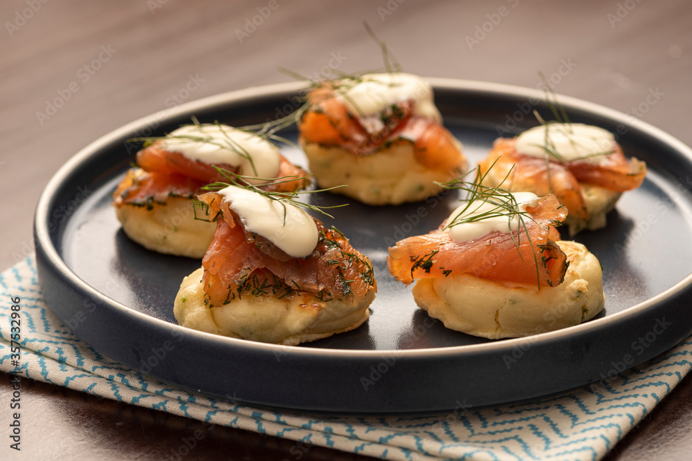 dried smoked salmon gravlax with dill and sour cream on blini pancake and blue ceramic plate and napkin on wooden table dried smoked salmon gravlax with dill and sour cream on blini pancake and blue ceramic plate and napkin on wooden table