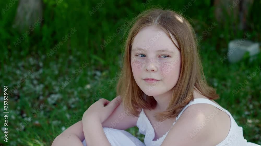 Portrait freckled girl teenager sitting on green grass in summer park. Face beautiful teen girl with freckles on skin in green park. Cute girl relaxing on summer meadow in shadow