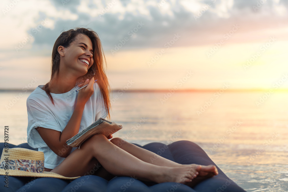 Young woman in straw hat talking to the smartphone and writing down on a beach. Young woman in straw hat talking to the smartphone and writing down on a beach.