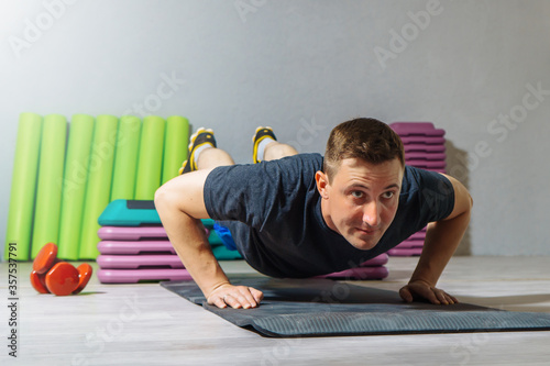Young caucasian man making push ups on a step platform in fitness studio. Healthy lifestyle concept.