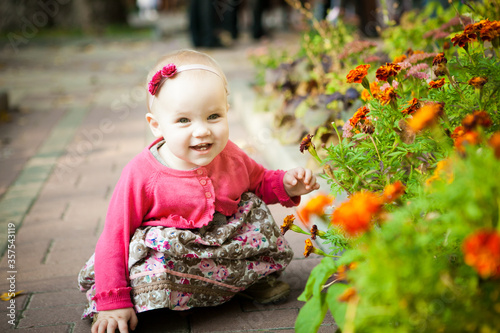 little girl in dress sitting on street near flower beds. walks in outdoors.