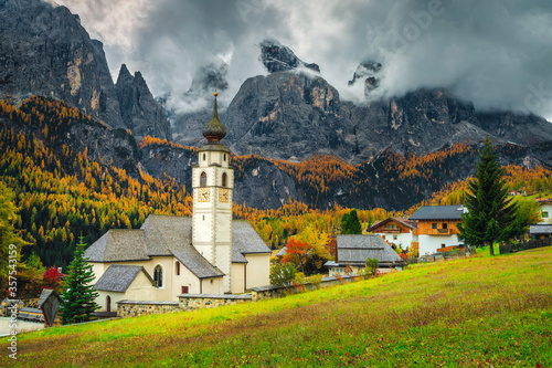 Traditional alpine church and street view with mountains, Dolomites, Colfosco photo