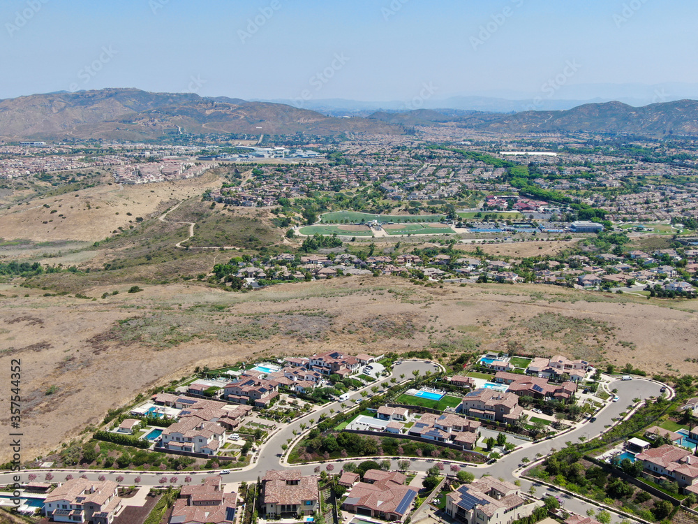 Aerial view of high class neighborhood with residential mansions and swimming pools in dry grass valley during hot summer. San Diego, California, USA.