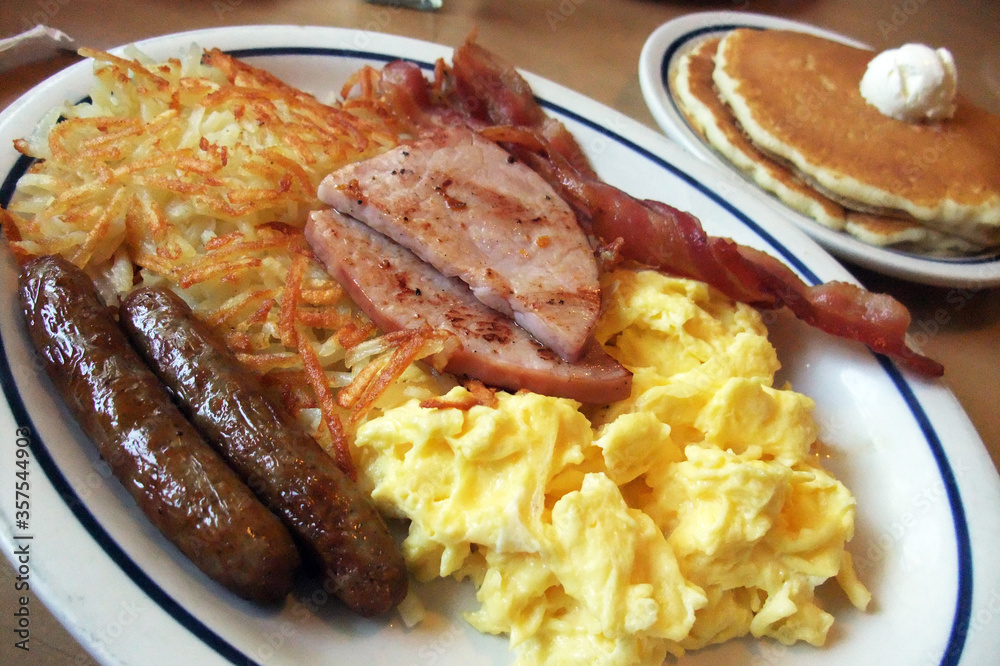 Full American Breakfast with sausage, ham, scambled egg, pancake and hash brown, served on oval china plate