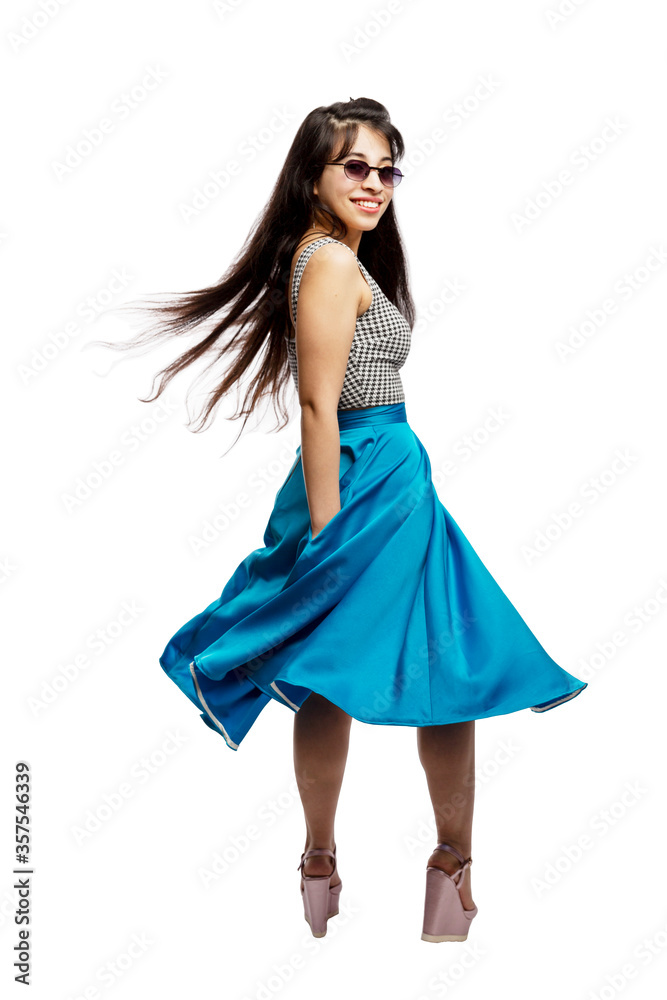 A young girl in a blue skirt and sunglasses laughs and dances. Brunette with long hair. Positive and emotions. Full height. Isolated on a white background. Vertical.