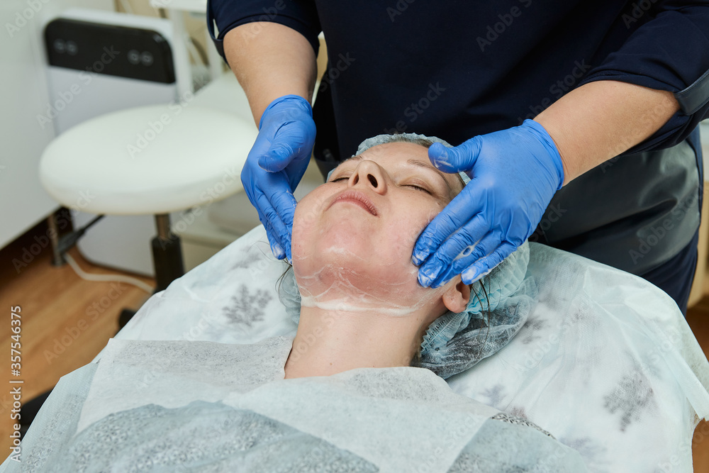 Doctor cosmetologist in gloves makes young woman massage procedure on the face with cream. Doctor cosmetologist in gloves makes young woman massage procedure on the face with cream.