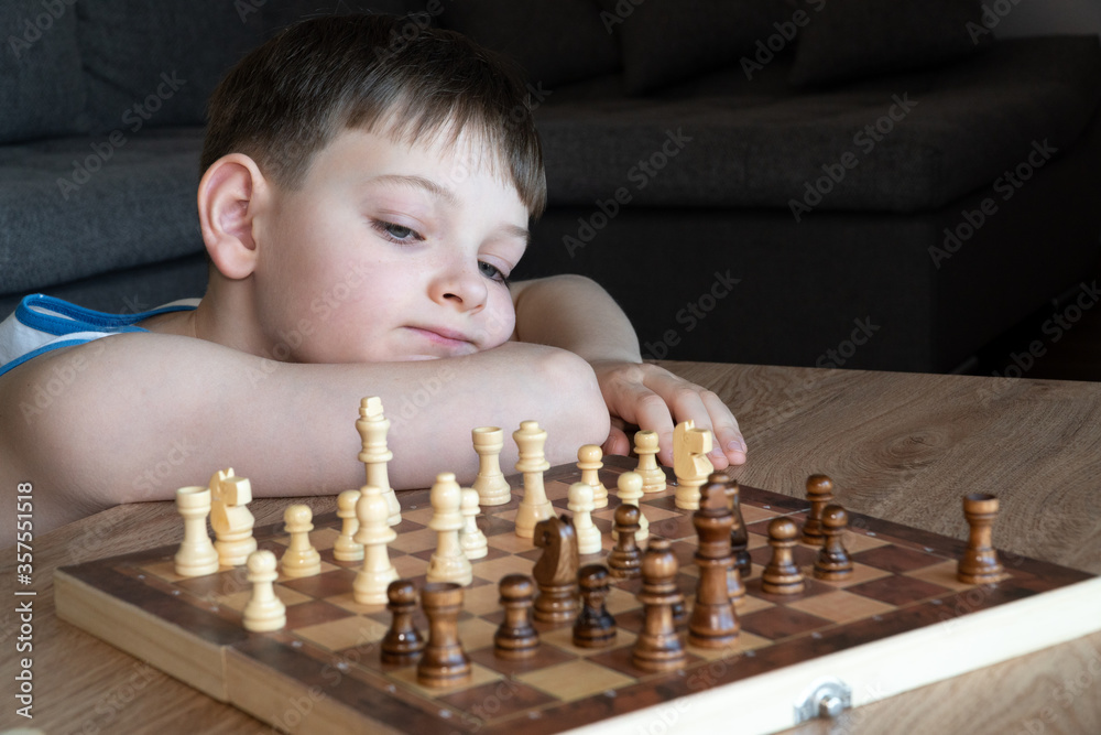 The serious child lost in thought playing chess. Playing board games, on coronavirus quarantine. The child playing chess.
