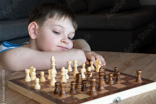 Obraz na płótnie The serious child lost in thought playing chess. Playing board games, on coronavirus quarantine. The child playing chess. w salonie