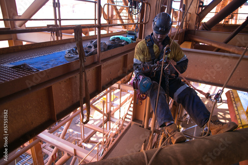 Industrial rope access rigger miner worker wearing safety harness, helmet working at height abseiling on twin ropes inspecting 3 tone chain block prior to used construction mine site Perth Australia 