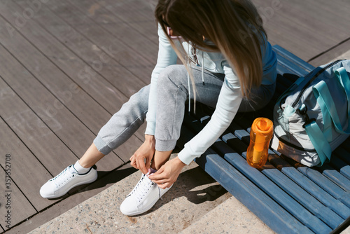 A young athletic woman preparing for training on the street  puts on sneakers and ties shoelaces. Healthy lifestyle concept. Street sport after quarantine by Covid-19 coronavirus