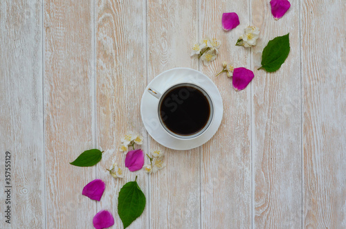 A cup of fresh black coffee with rosehip petals and white spring flowers top view on a wooden table. Good morning and breakfast. Copy space for text
