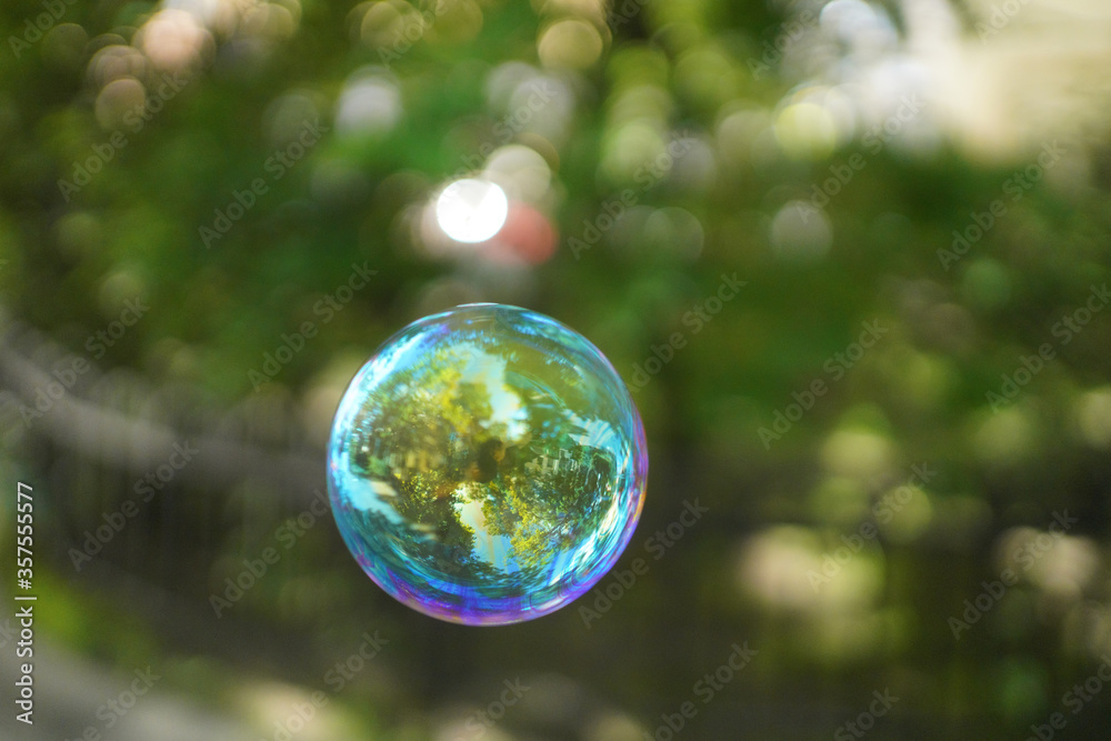 Colored iridescent soap bubble in the air with reflections. On blurred background Colored iridescent soap bubble in the air with reflections. On blurred background
