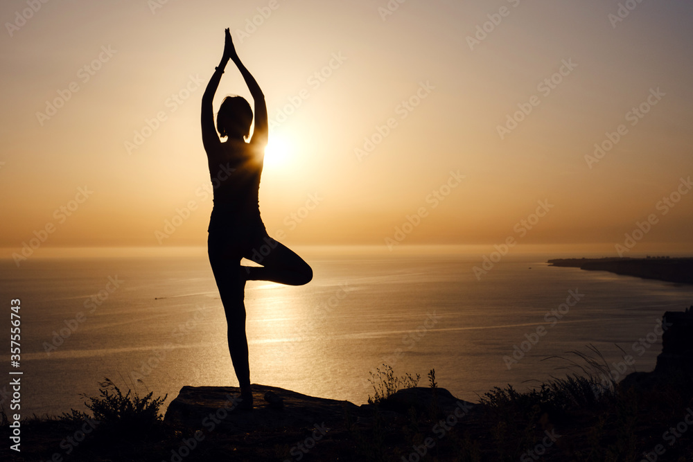 The woman with yoga posture on the mountain at sunset