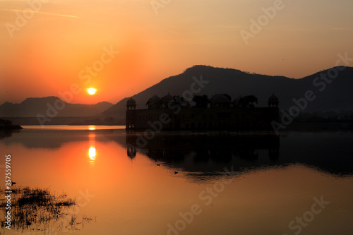 A view of Sunrise.Sun rising from behind the Hills and showing its reflection in the water of the lake. 