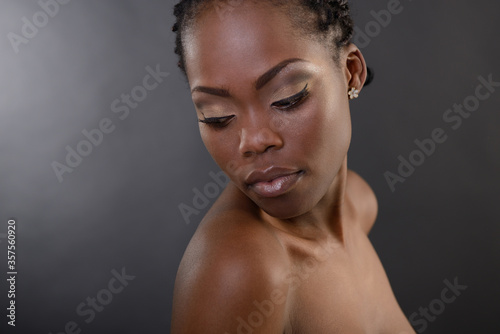 Gorgeous young african american woman looking down st copy space, over black background. Beauty portrait of charming girl with clean skin, studio shot