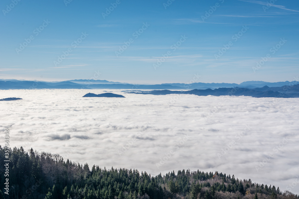 Aerial view inversion fog in the valley. Amazing mountain landscape in Slovenia. Hiking on hilltop. Bright sunny day over the clouds