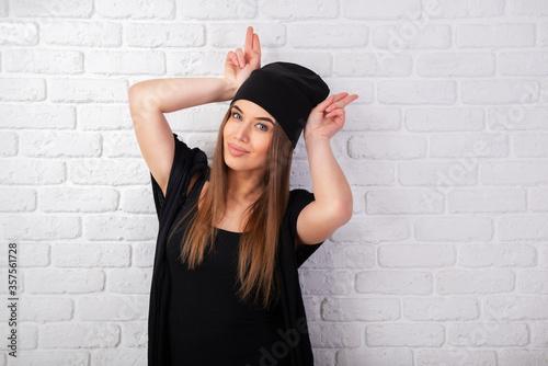 Portrait of young attractive cheerful woman wearing black clothes makes faces, studio shot over white bricks background. Pretty girl has fun, studio shot