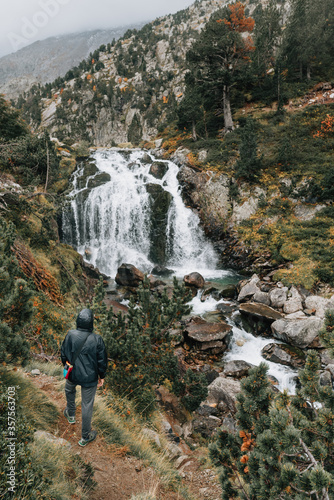 Lonely man watching a waterfall in nature of Benasque Valley, surrounded by the highest peaks in that range, located in the heart of the Pyrenees, Aragón, Spain