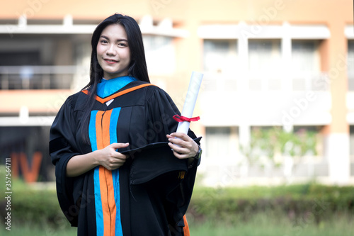 Portrait of a happy and excited young Asian female university graduate wears graduation gown and hat celebrates with a degree in the university campus on the commencement day. Education concept.