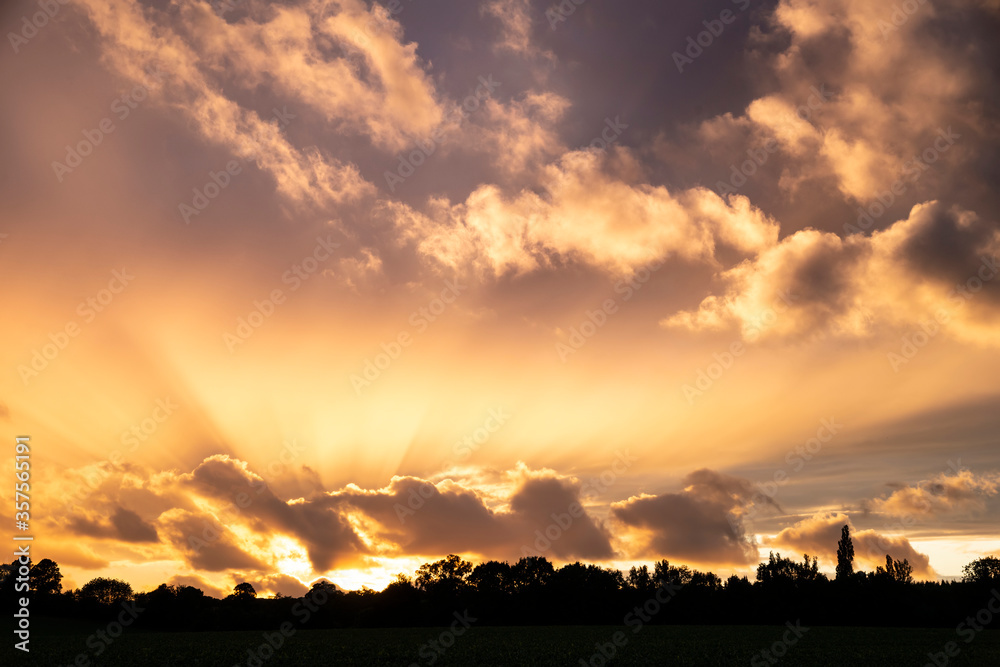 Stunning Summer sunset sky with colorful vibrant clouds and sun beams across whole sky