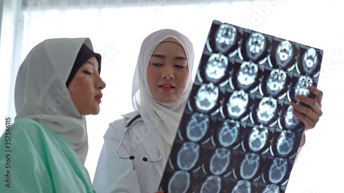 Woman muslim doctors shows at an X-ray of the found problem of patient and explains the cause of her pain.