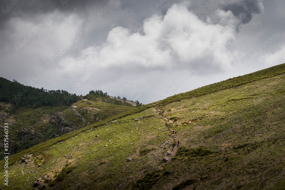 Hikers go up a hill under cloudy skies Hikers go up a hill under cloudy skies