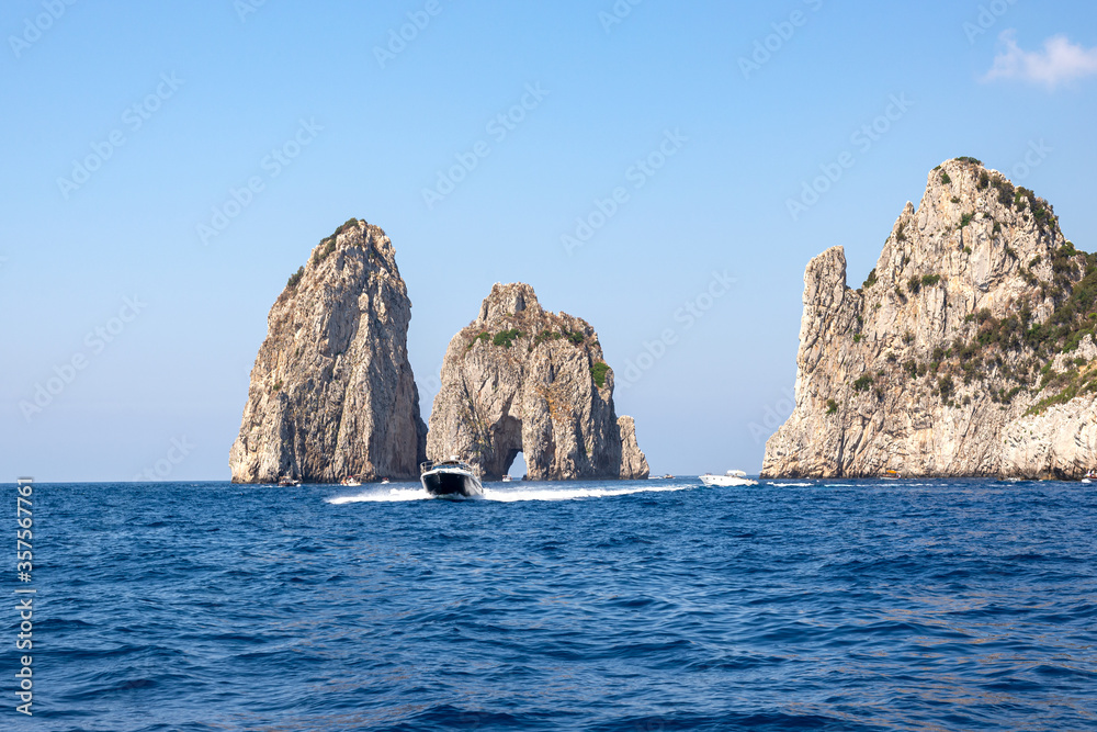 The blue sea and the faraglioni of Capri with a yacht in the foreground. Summer mood in Italy