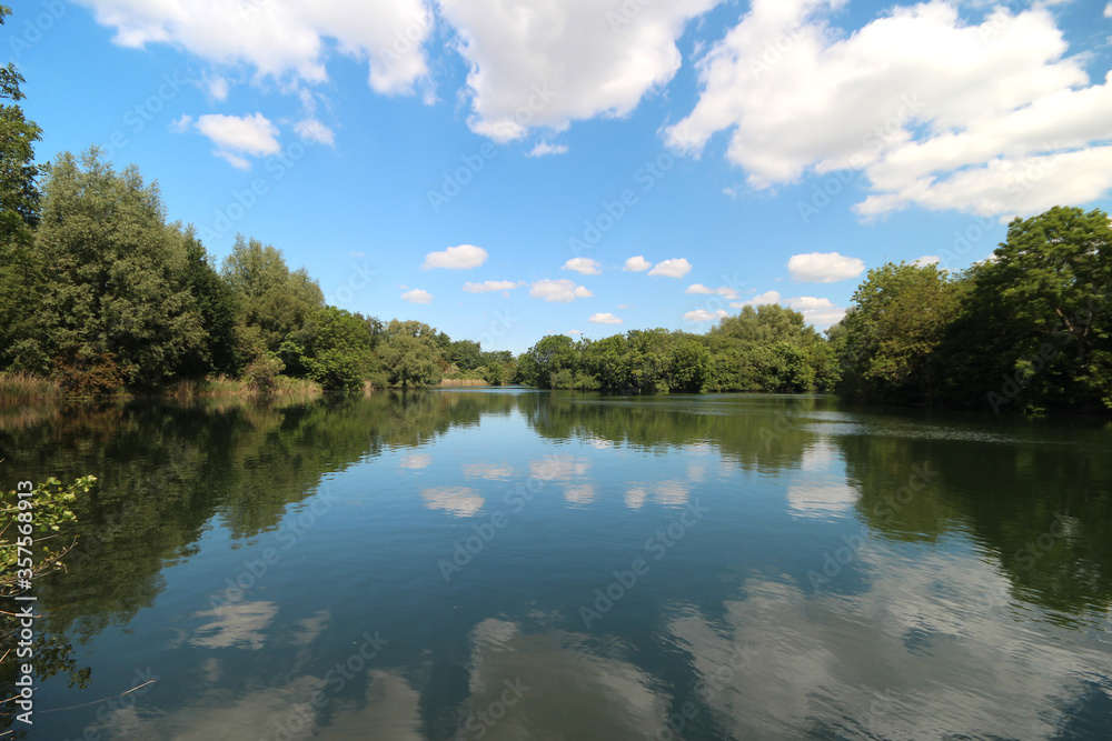 White cumulus clouds and blue sky reflecting on the water surface of the Zevenhuizerplas White cumulus clouds and blue sky reflecting on the water surface of the Zevenhuizerplas