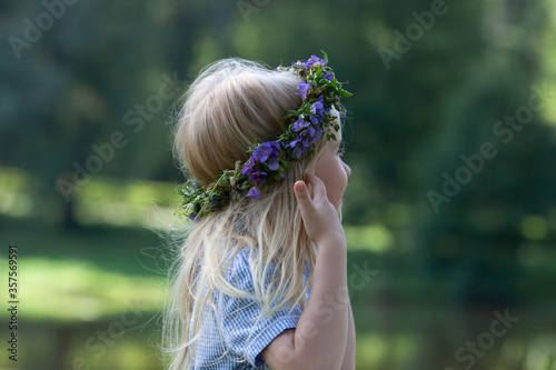 Little blond girl with the wreath of blue wild flowers. side view. The celebration of Ivan Kupala (St. John Day). Old holiday dedicated to the summer solstice. Selective focus. photo