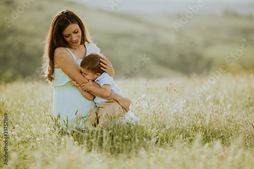 Young pregnant mother with her cute little boy in the field on beautiful sunny day