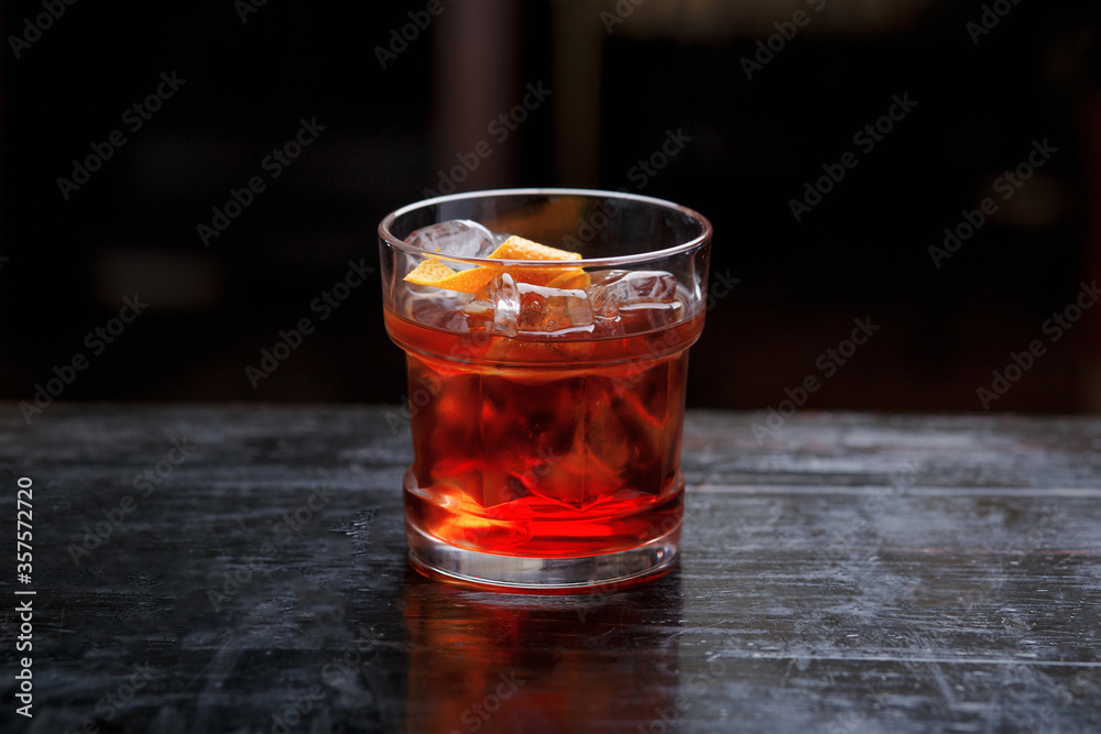 Horizontal view. Closeup of a God father cocktail in short glass, gin, standing on the bar counter, isolated on a red light background. Horizontal view. Closeup of a God father cocktail in short glass, gin, standing on the bar counter, isolated on a red light background.