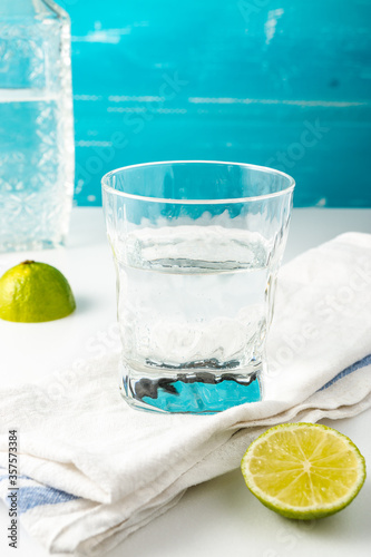 Cold summer delicious coctail with lime and ice in a glass with drops on the white and blue background.