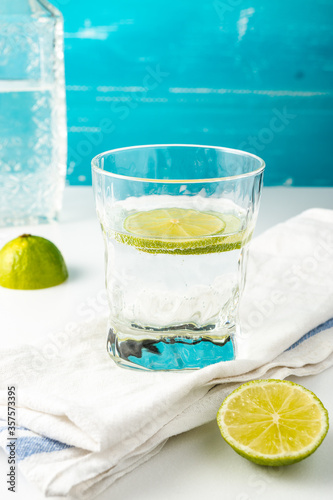 Cold summer delicious coctail with lime and ice in a glass with drops on the white and blue background.