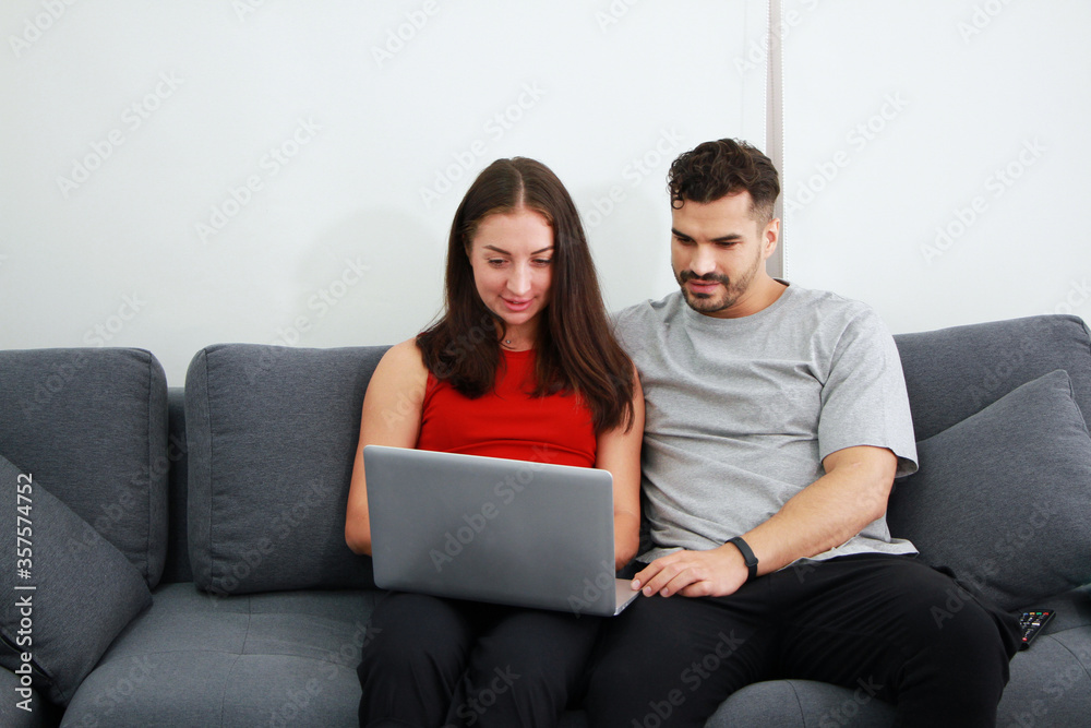 Smiling Caucasian Couple sitting on sofa and working for online business on laptop in social media technology . Work from home and Covid 19 virus is spreading around the world Concept. Smiling Caucasian Couple sitting on sofa and working for online business on laptop in social media technology . Work from home and Covid 19 virus is spreading around the world Concept.