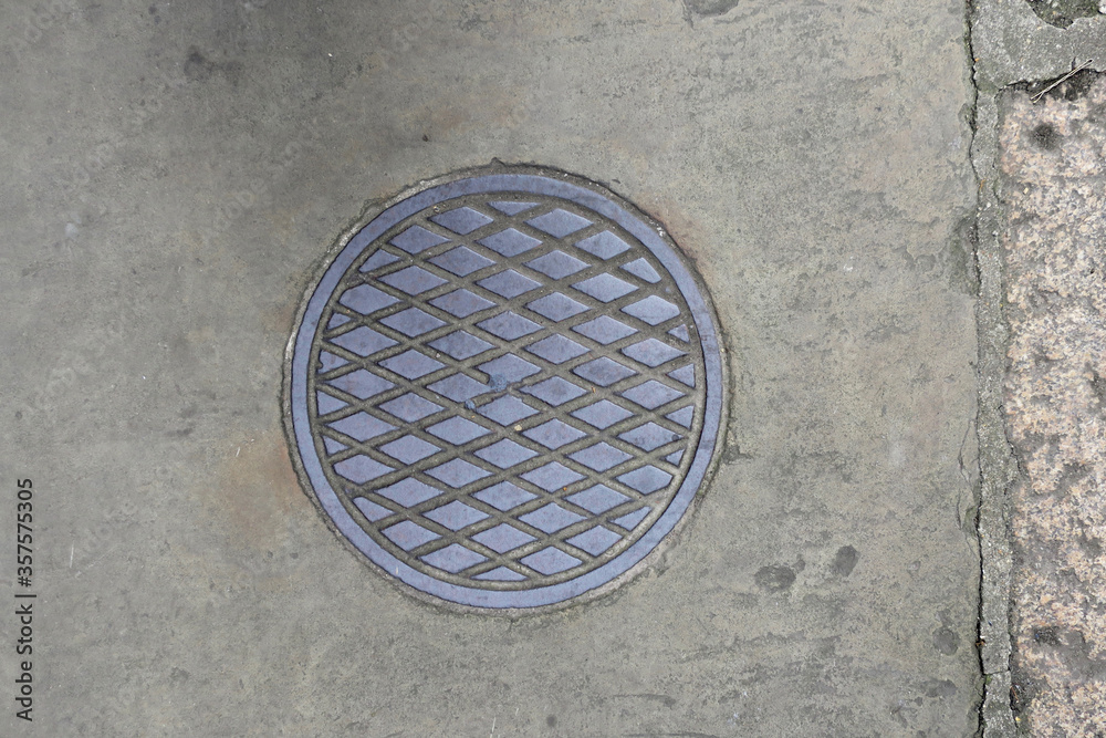 round manhole cover witj a diamond pattern on the sidewalk round manhole cover witj a diamond pattern on the sidewalk