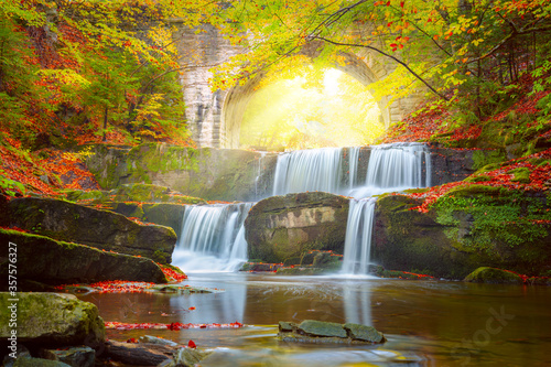 Sunny Autumn landscape - river waterfall in colorful autumn forest with old bridge