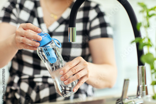 Woman screw the bottle on. Woman screws on the reusable bottle of water with carbon filter in the kitchen