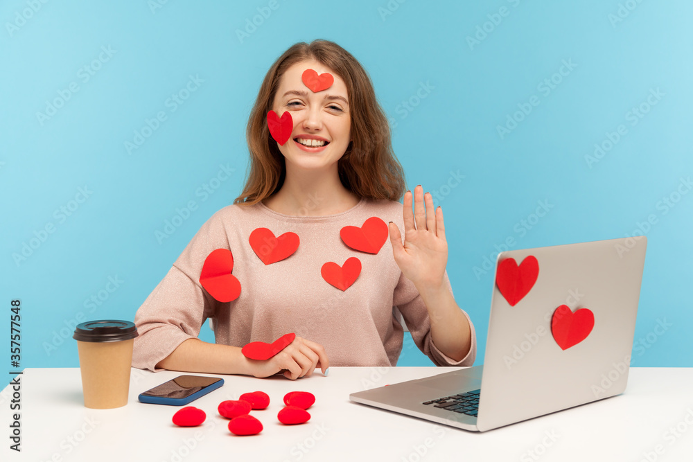 Hi, welcome, nice to meet! Amazing cheerful woman with kind smile sitting at workplace office, all covered with sticker love hearts, gesturing hello. indoor studio shot isolated on blue background Hi, welcome, nice to meet! Amazing cheerful woman with kind smile sitting at workplace office, all covered with sticker love hearts, gesturing hello. indoor studio shot isolated on blue background