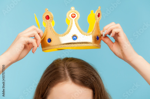 Closeup of woman putting on head golden crown, concept of awards ceremony, privileged status, superior position, self-motivation and big ambitions to achieve success. indoor studio shot, isolated photo