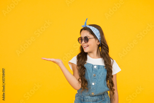 retro girl presenting product. small kid wear summer outfit. cheerful child has vintage look. headkerchief and sunglasses - summer accessory. beauty and fashion. happy childhood. copy space photo