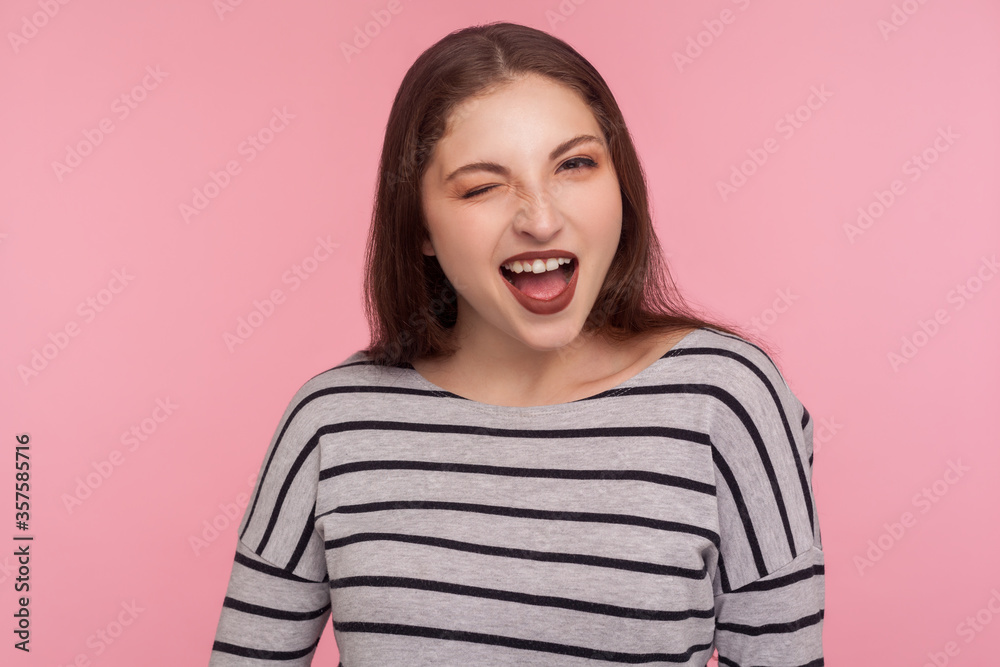 Portrait of coquettish playful beautiful woman in striped sweatshirt flirting to camera, blinking eye and looking carefree, cheering up with wink. indoor studio shot isolated on pink background Portrait of coquettish playful beautiful woman in striped sweatshirt flirting to camera, blinking eye and looking carefree, cheering up with wink. indoor studio shot isolated on pink background