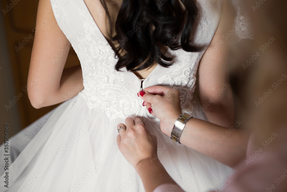 Female hands button the wedding dress to the bride with a beautiful hairstyle