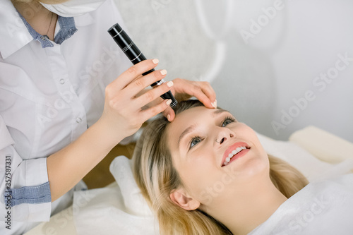 Cropped image of female doctor dermatologist examining face skin of pretty blond girl patient with dermatoscope. Skin checkup. Professional dermoscopy