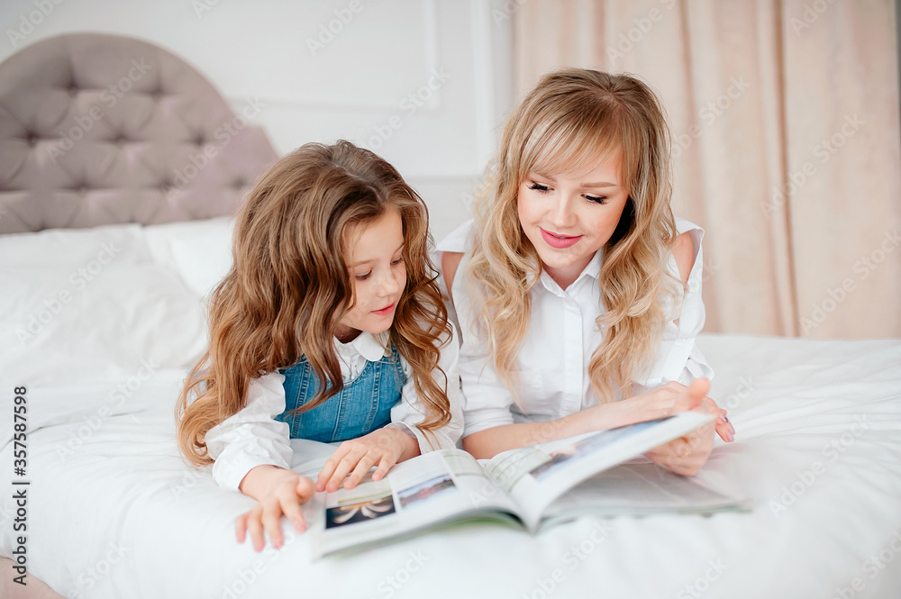 Happy family mother and child daughter reading holding book lying in bed, smiling mom baby sitter telling funny fairy tale to cute preschool kid girl Happy family mother and child daughter reading holding book lying in bed, smiling mom baby sitter telling funny fairy tale to cute preschool kid girl