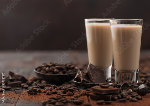 Irish cream baileys liqueur in shot glasses with coffee beans and powder with dark chocolate on dark wood background.