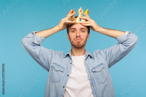 I'm ceo! Portrait of worker man wearing golden crown, imagining promotion at work to position of top manager or boss, looking with arrogance, privileged status. studio shot isolated on blue background photo