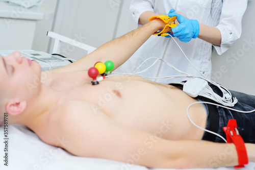 doctor of cardiology - a young pretty woman puts rubber vacuum electronic sensors for ECG or electrocardiogram on the body of a male patient. Prevention of cardiovascular diseases