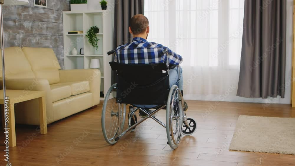 Back view of man with walking disability sitting on wheelchair. Handicapped invalid paralysed person, alone at home, depression and health problems, pensive, sad and unhappy man Back view of man with walking disability sitting on wheelchair. Handicapped invalid paralysed person, alone at home, depression and health problems, pensive, sad and unhappy man