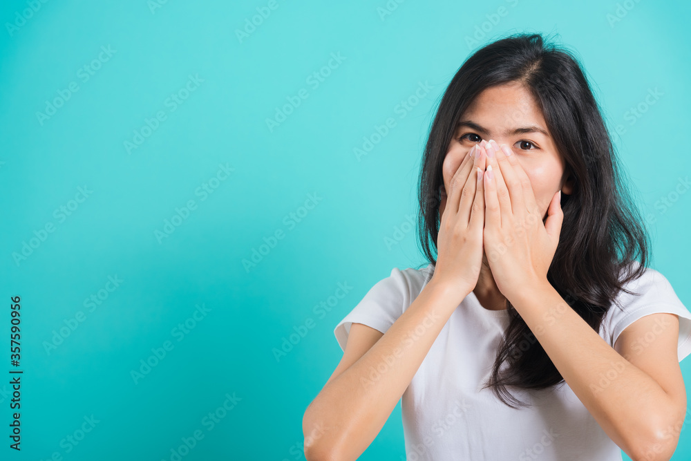 Portrait Asian beautiful happy young woman wear t-shirt happy excited laughs covering mouth with hands, on a blue background, with copy space Portrait Asian beautiful happy young woman wear t-shirt happy excited laughs covering mouth with hands, on a blue background, with copy space