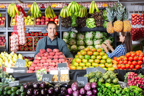 Friendly man and woman laying out vegetables and fruits in shop